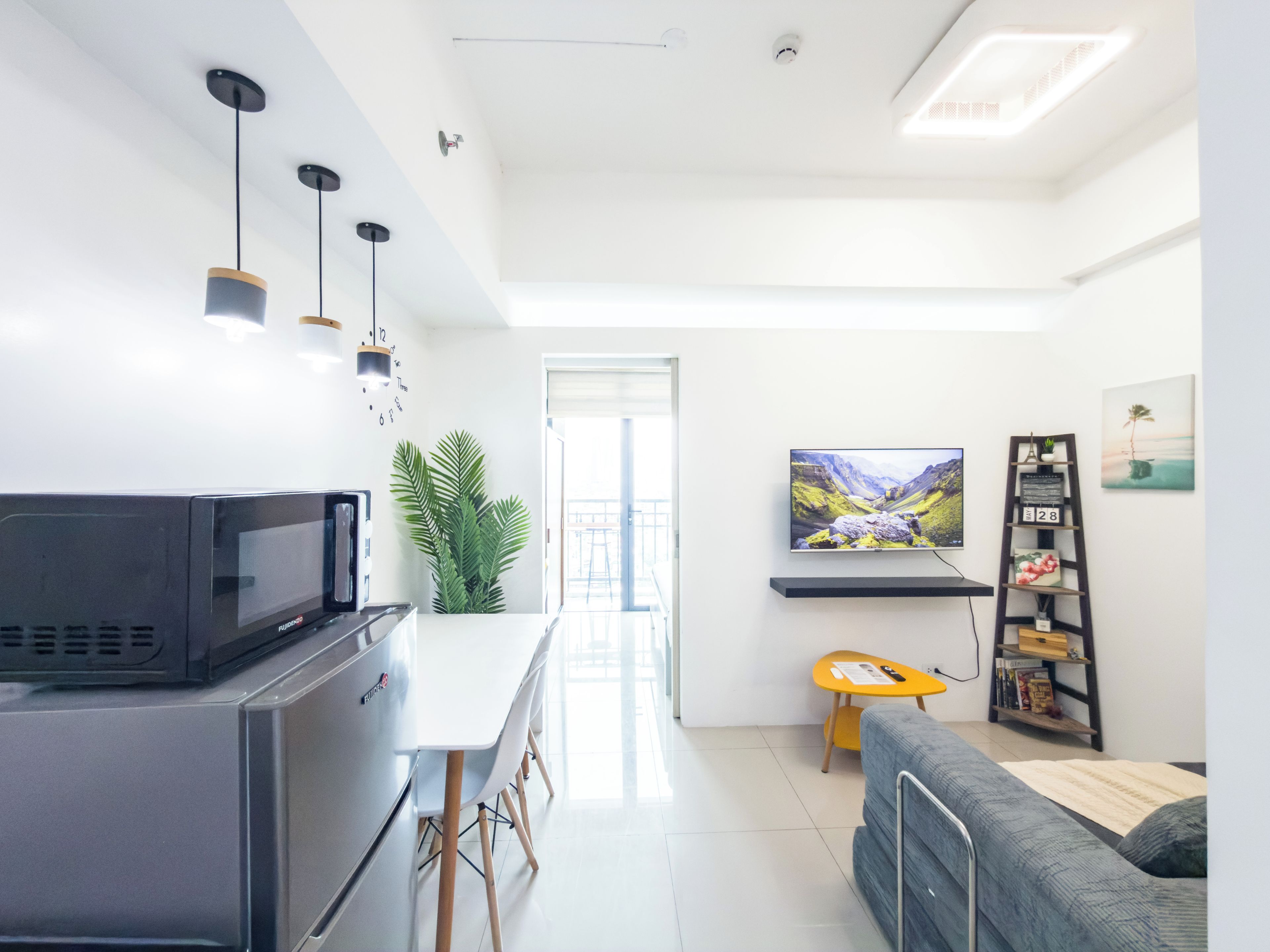 Una cocina moderna con microondas, un comedor con mesa y sillas blancas, un sofá, un televisor y una estantería con objetos decorativos.