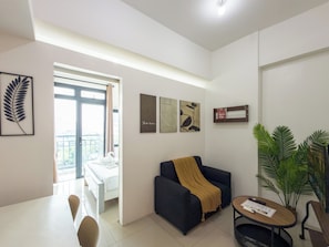 A modern living room with a sofa, a coffee table, and a dining area with chairs. There are framed artworks on the wall and a potted plant. - GemstoneBR in Harbour Park Residences (Mandaluyong City)