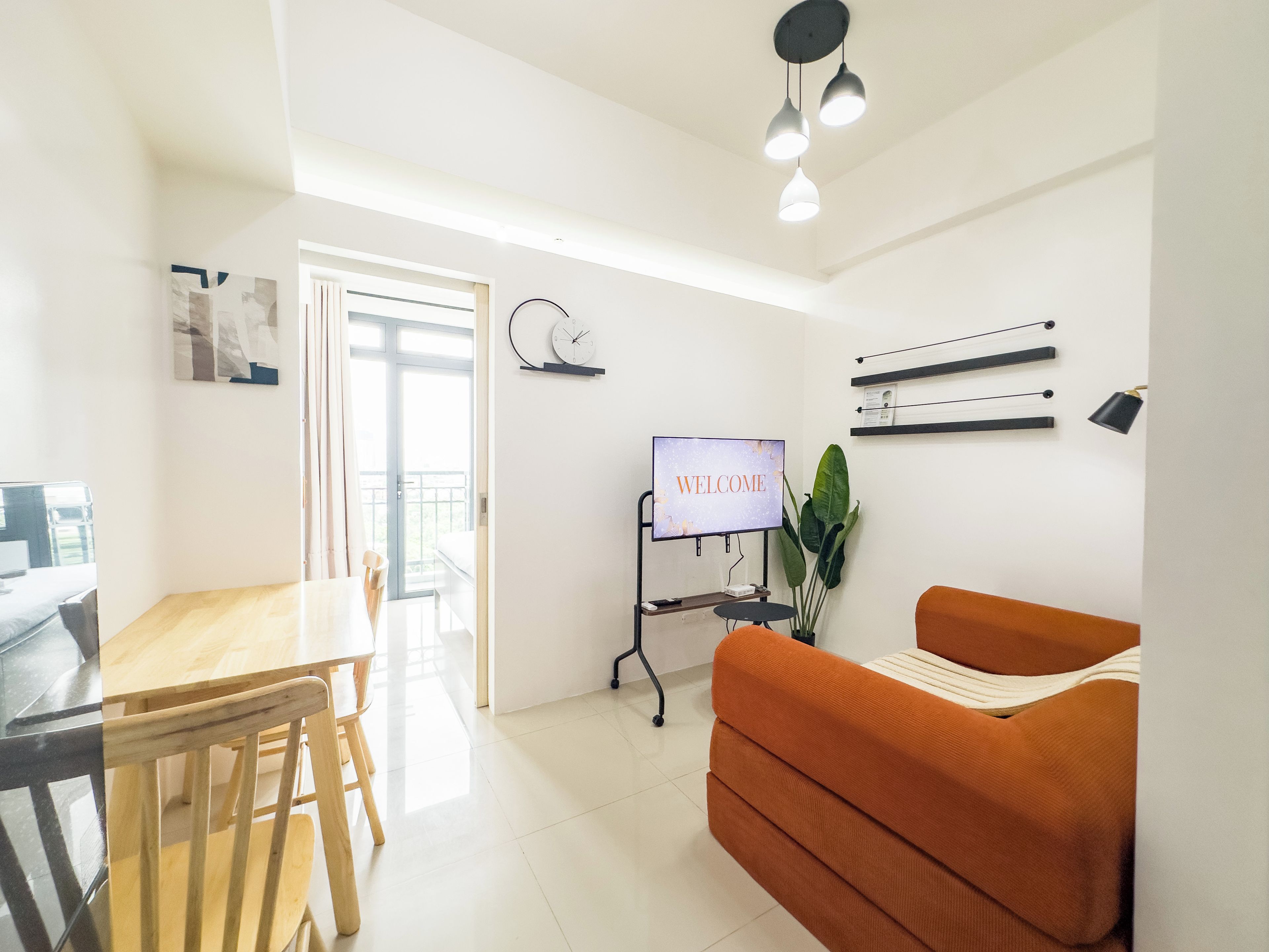 Una sala de estar moderna con un sofá, una mesa de comedor y una pantalla de televisión mostrando 'WELCOME'.