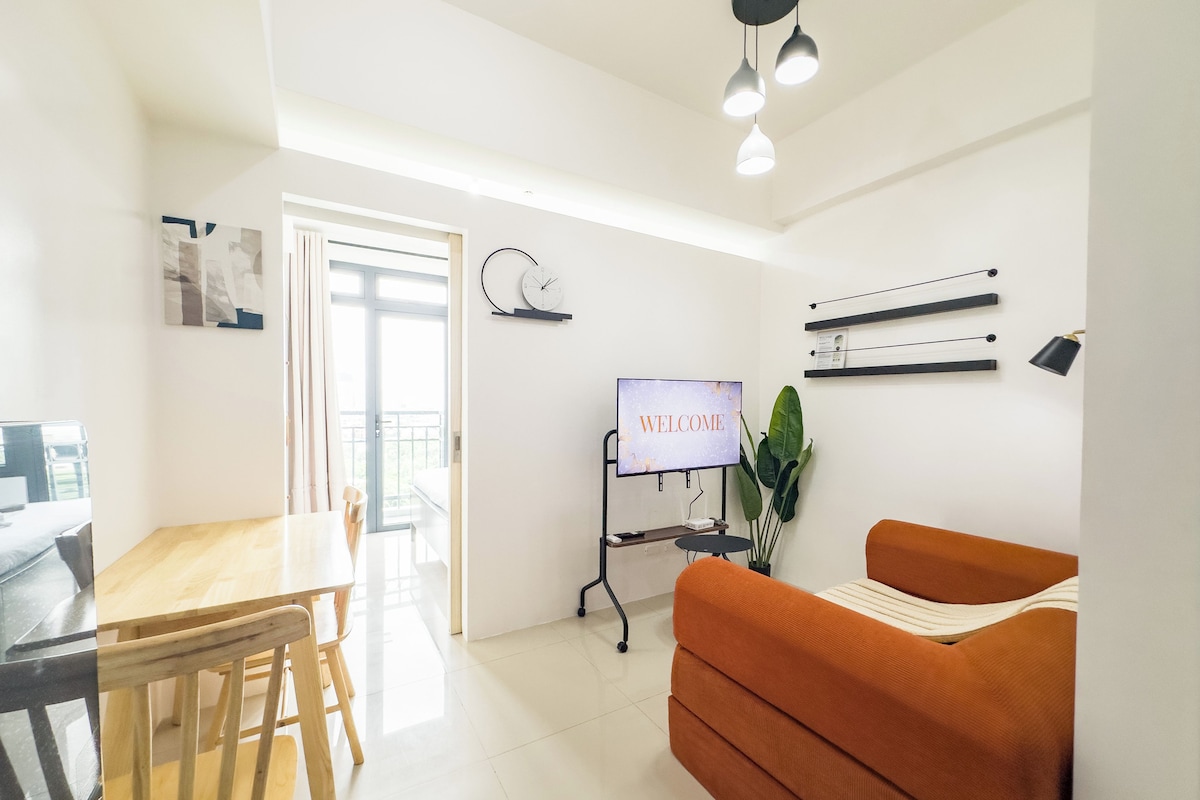 Una sala de estar moderna con un sofá, una mesa de comedor y una pantalla de televisión mostrando 'WELCOME'.