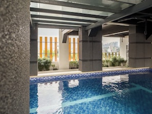 Una piscina con agua cristalina azul, rodeada por un borde de azulejos y sostenida por pilares de hormigón.