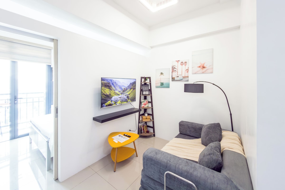 Una sala de estar moderna con un televisor de pantalla plana, un sofá, una mesita amarilla y una estantería.