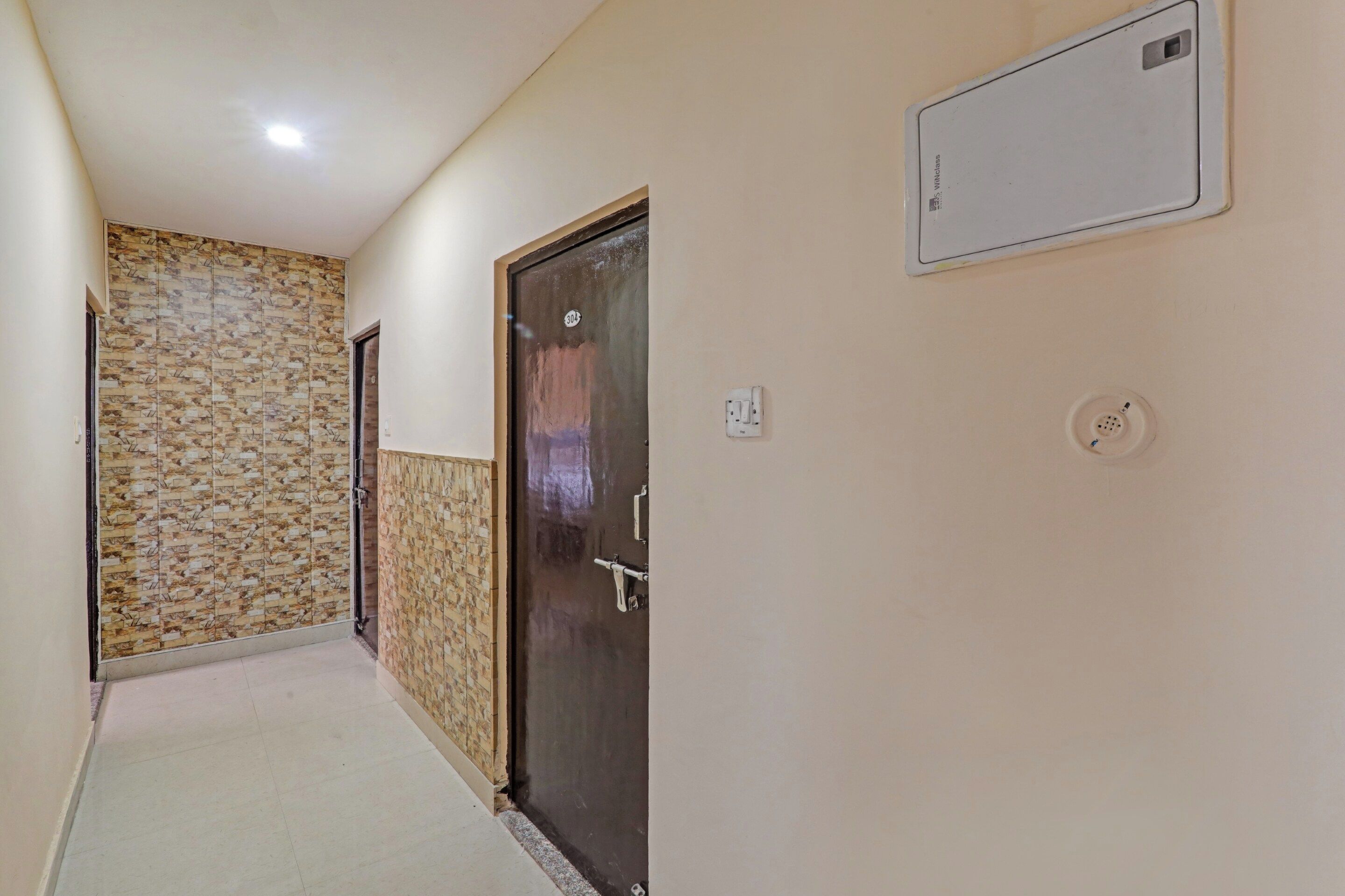 Un pasillo con un papel tapiz estampado, una puerta con placa de número y un cuadro de empalmes eléctricos en la pared.