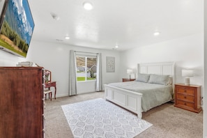 A bedroom with a bed, bedside tables, a dresser, a television, and a window with a view of houses. - Luxury Mountain View Retreat (Santaquin)