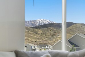A view from a window overlooking a mountain with snow-capped peaks, a residential area with houses, and a clear sky. - Luxury Mountain View Retreat (Santaquin)