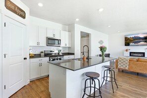A modern kitchen with white cabinetry, a central island with stools, a microwave, and a stove.