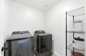 A laundry room with two black washing machines, a metal shelf with a jar and a pot, and a white wall. - Luxury Mountain View Retreat (Santaquin)