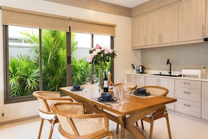Una cocina moderna con una mesa de comedor lista para cuatro personas, rodeada de armarios de colores claros y un amplio ventanal con vistas a zonas verdes.
