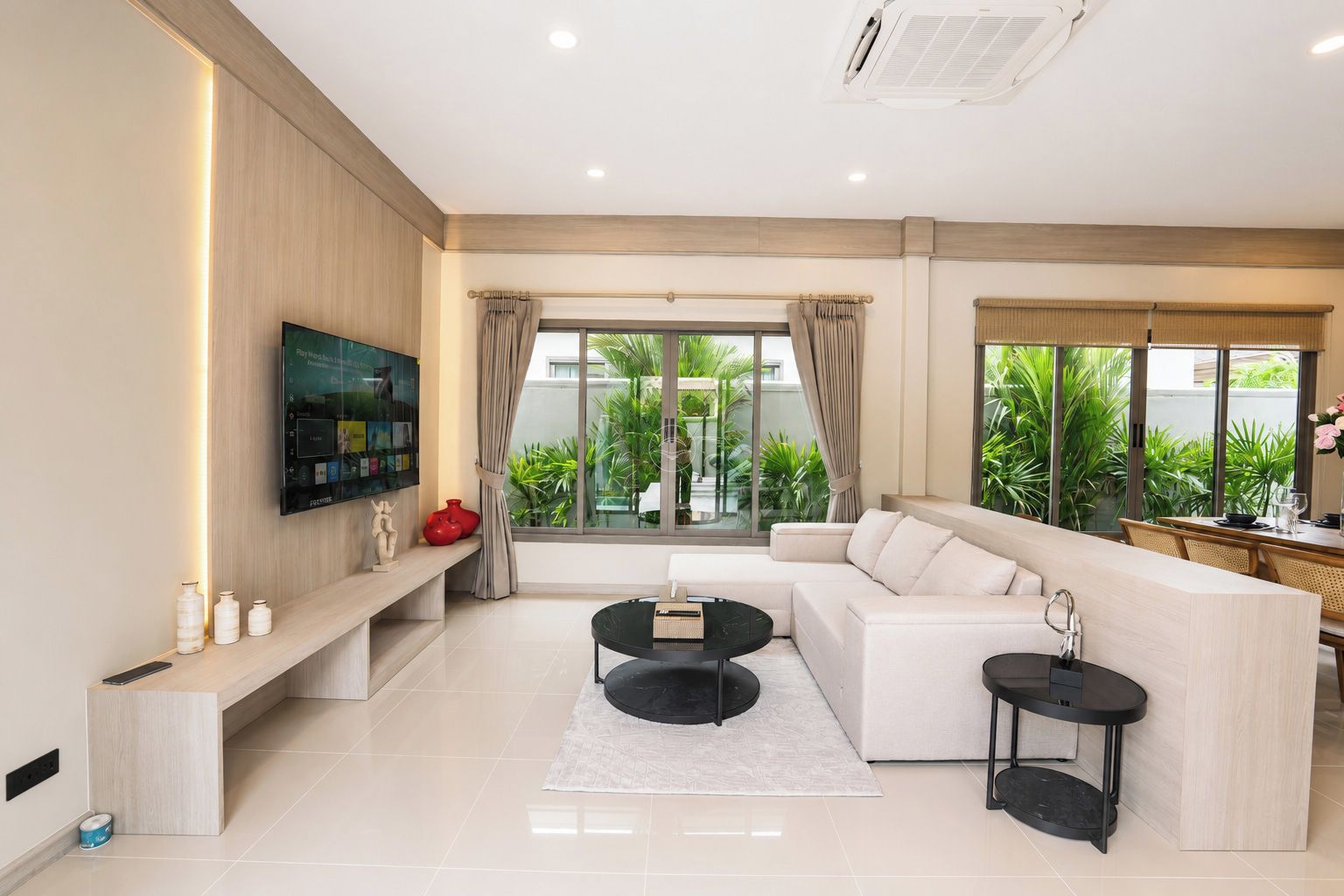 A modern living room with a flat-screen TV, a sofa, two side tables, and a dining area with a table and chairs.