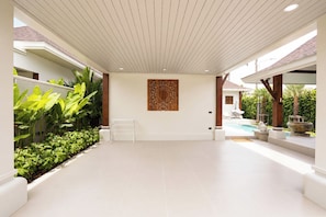 Un espacio interior amplio con suelo de baldosas, un banco blanco, una obra de arte colgada en la pared y una zona de piscina con sillones de descanso.