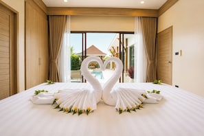 Habitación de hotel con cama, dos toallas con forma de cisne y vistas a una piscina y zona exterior.
