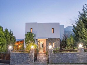 A modern two-story building with a stone facade, a wooden gate, and a pathway leading to the entrance. - Peaceful Pool Villa in Crete Countryside (Apokoronas)