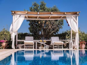 A poolside area with a pergola, two lounge chairs, and a clear blue pool. - Peaceful Pool Villa in Crete Countryside (Apokoronas)