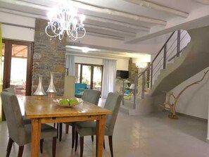 A dining area with a wooden table and chairs, a chandelier, and a stone wall. - Peaceful Pool Villa in Crete Countryside (Apokoronas)