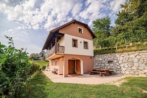 A two-story building with a balcony, a stone wall, and a grassy area with a bench.