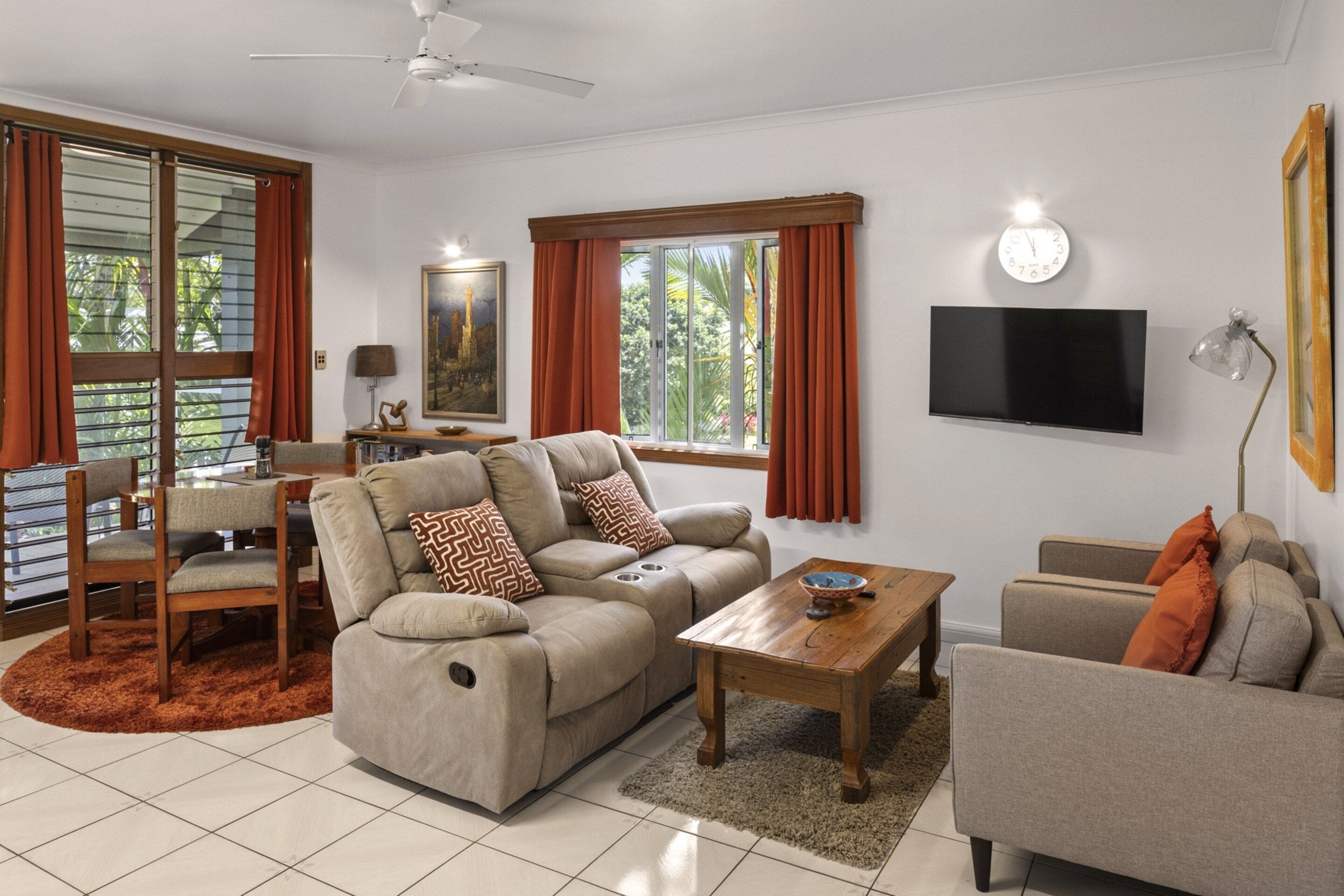 A modern living room with a sofa, armchairs, a coffee table, a TV, and a ceiling fan.