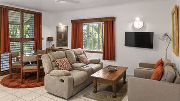 A modern living room with a sofa, armchairs, a coffee table, a TV, and a ceiling fan.