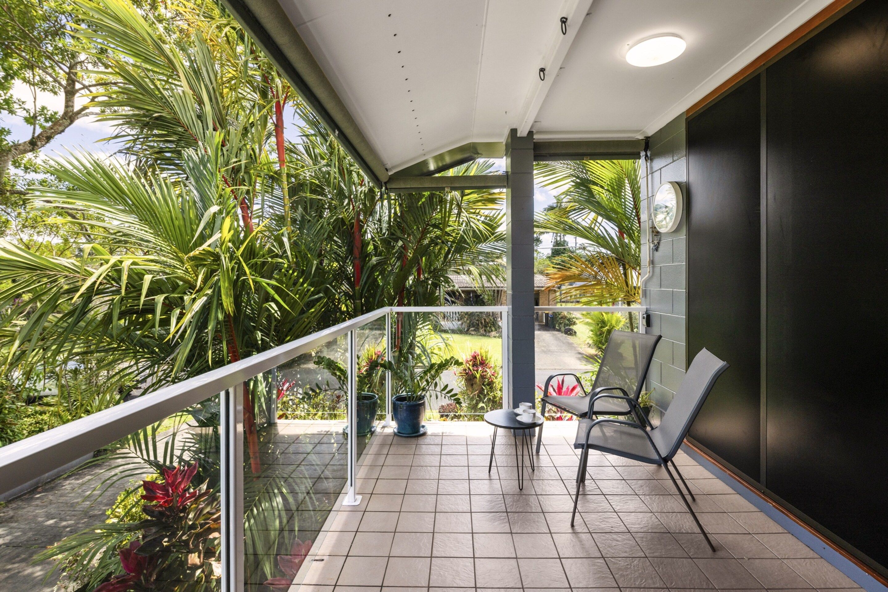 A balcony with a glass railing, a small table, two chairs, and potted plants.