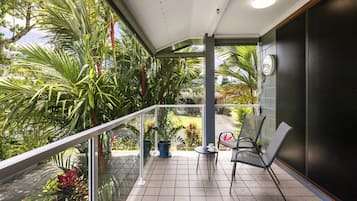 A balcony with a glass railing, a small table, two chairs, and potted plants.