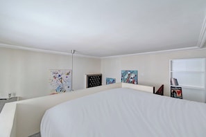 Ein Hotelzimmer mit Bett, Schreibtisch, Stuhl, Stehlampe und Kunstwerken an den Wänden.