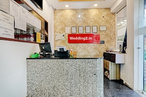 A reception desk with a computer, a check-in counter, and a wall with framed certificates and emergency contact information. - Townhouse Jayati Oasis Inn (Lucknow)