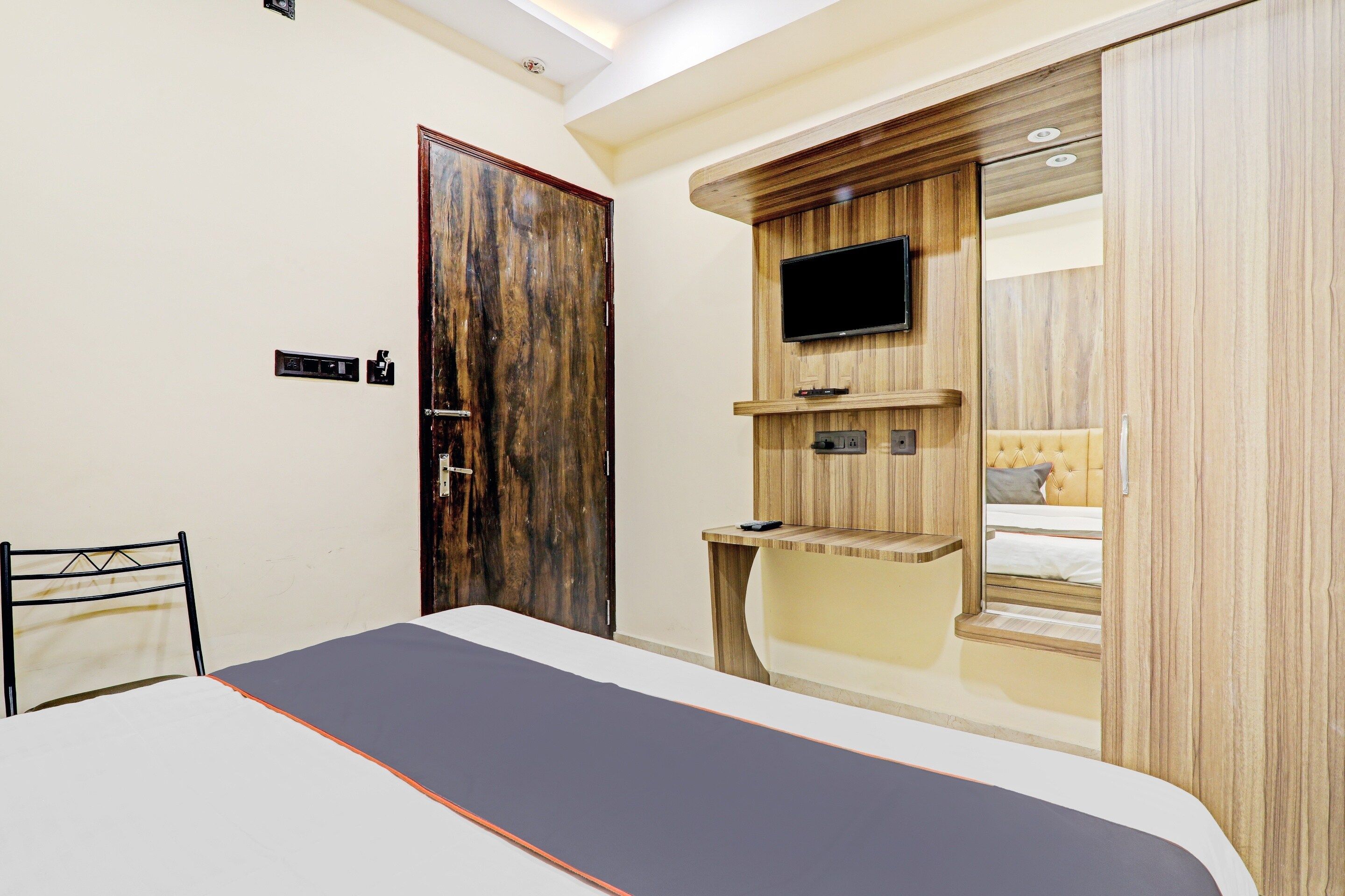 Un dormitorio con una cama, un televisor montado en un mueble de madera, un armario y una silla.