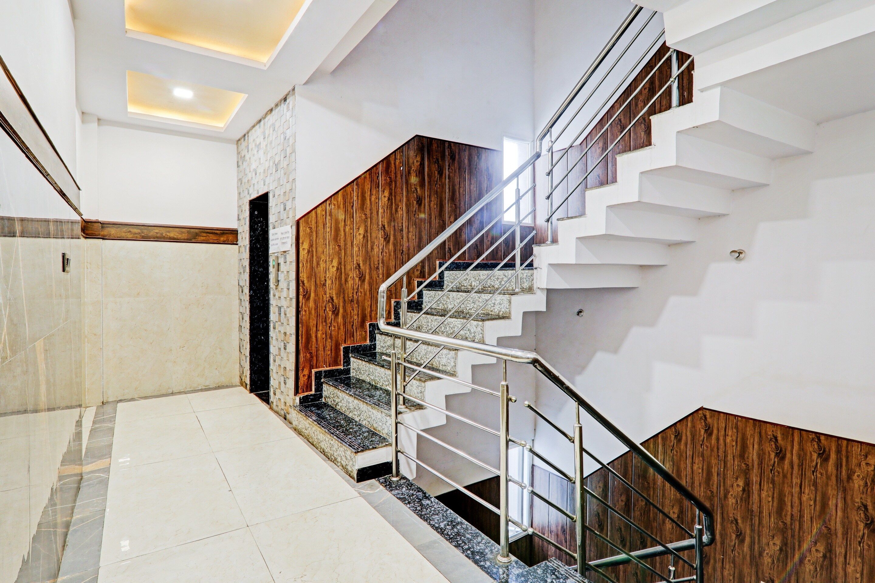 Una escalera moderna con detalles de madera y barandales de metal, que conduce a un rellano con piso de baldosas.