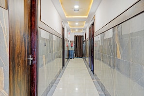 A corridor with marble walls and doors, leading to a room with a fire extinguisher and a blue object on the floor. - Townhouse Jayati Oasis Inn (Lucknow)