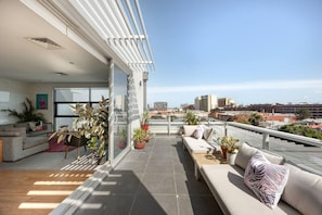 A modern living room with a sofa and a dining area, connected to a balcony with potted plants and a city view. - Parking included - unrivalled views of Kensington (Kensington)