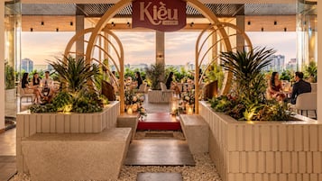 Un espai interior modern amb una arc central que porta la inscripció 'Kiêu by KITA', envoltat d'espais d'seure amb plantes i vista a la ciutat.