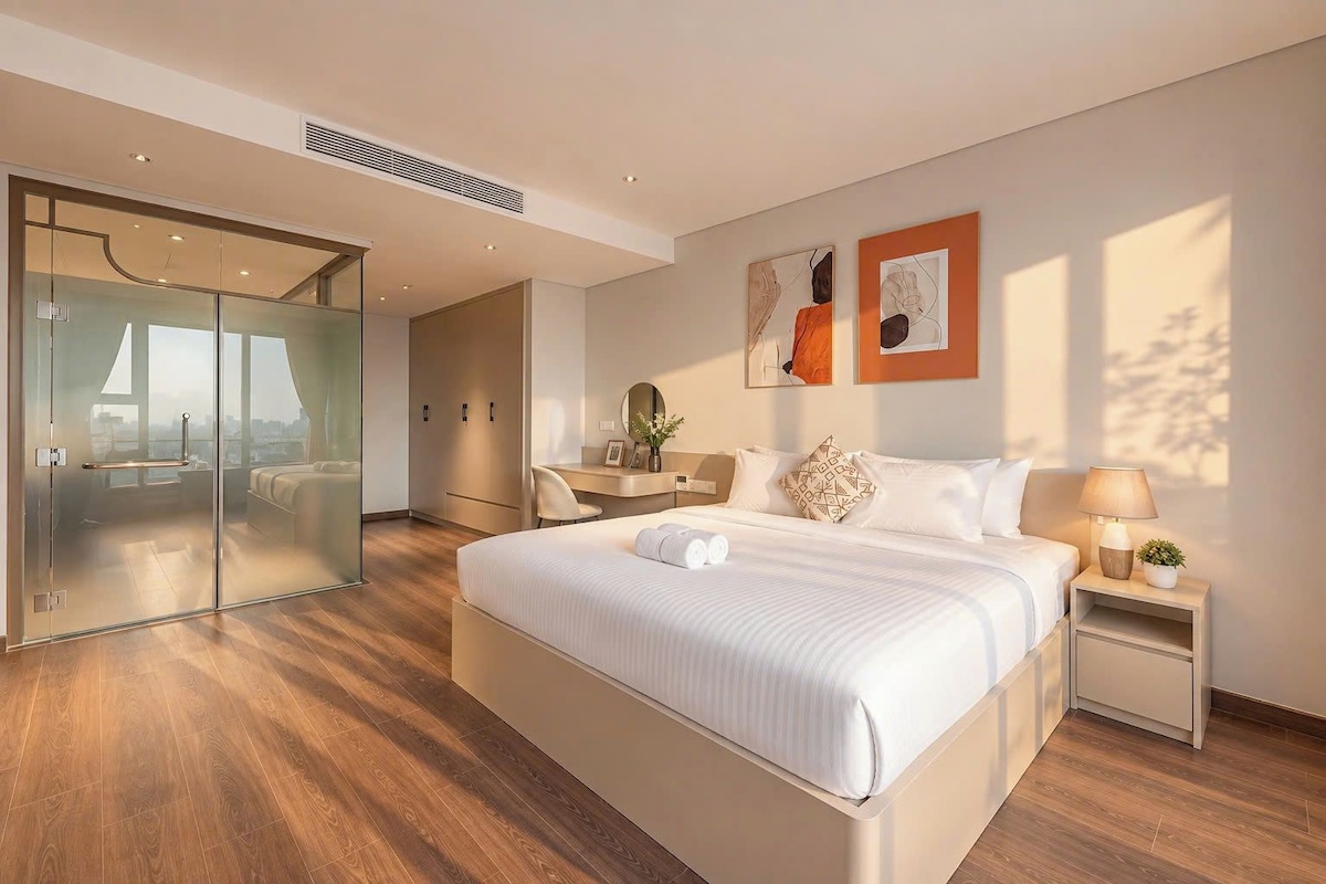 Una habitación de hotel moderna con una cama grande, un escritorio, una silla, una mesita de noche y vistas a través de una puerta de cristal.