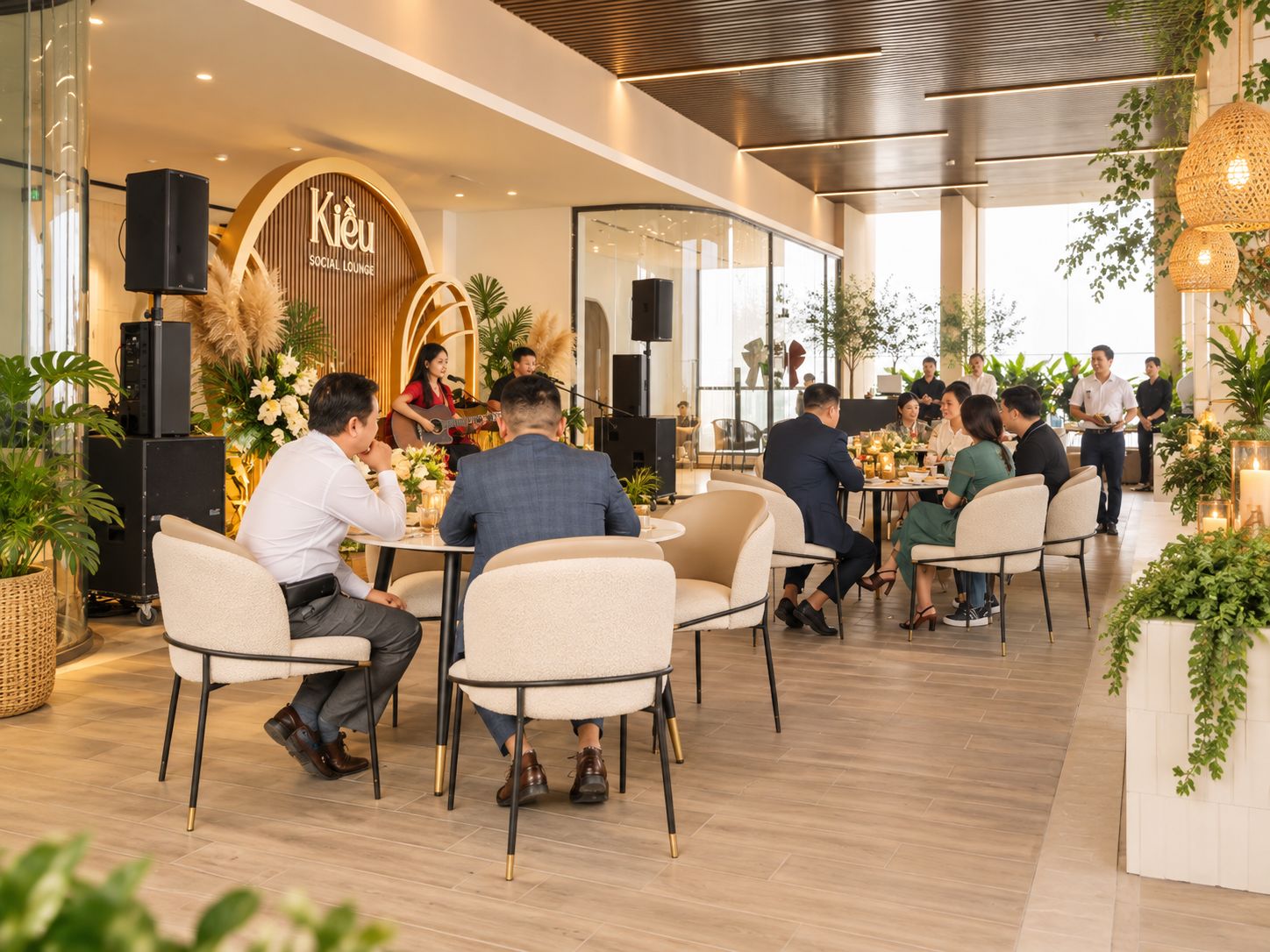 A social lounge area with round tables and chairs, a stage with a guitarist, and a modern interior design.