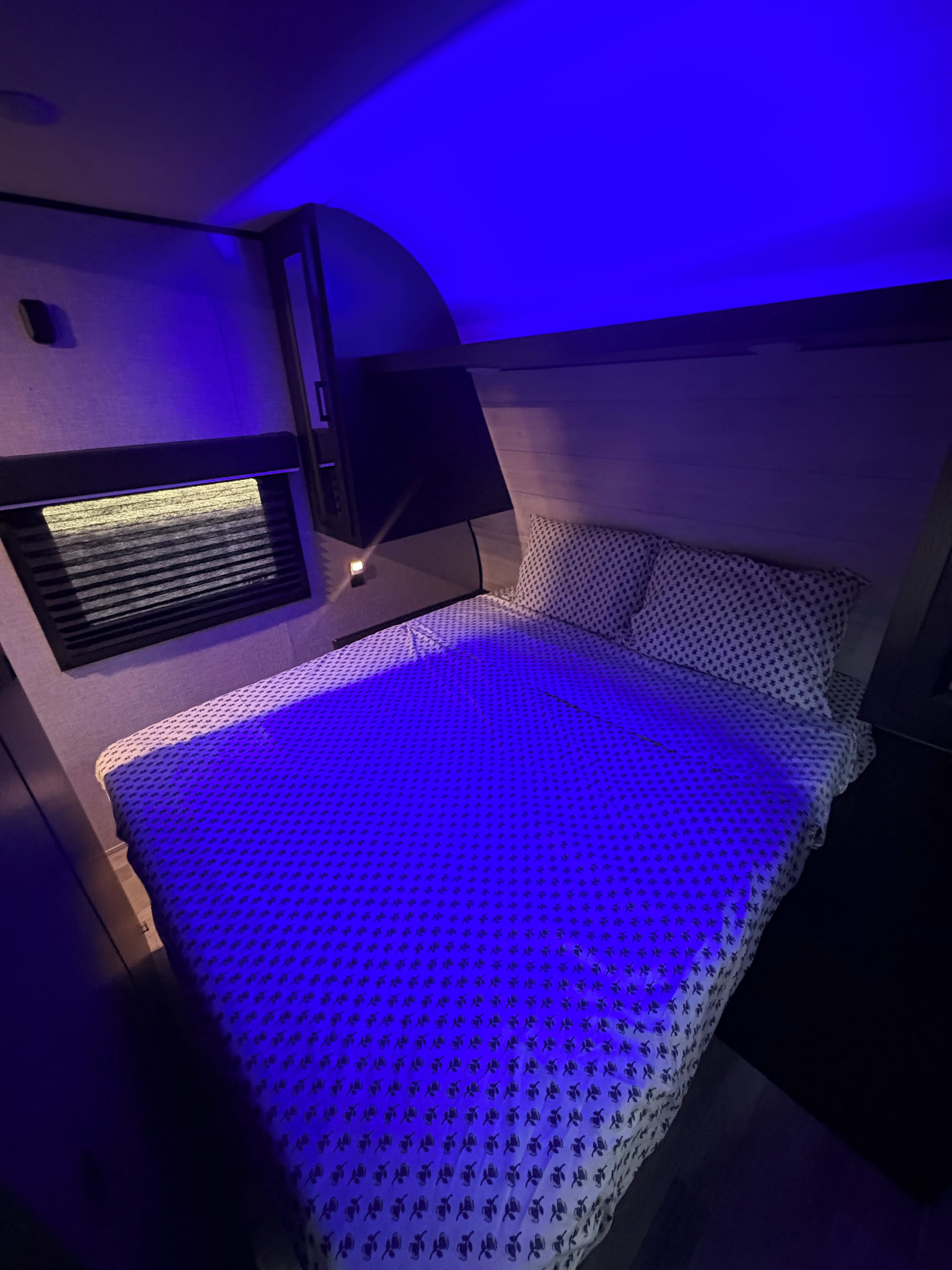 Un lit avec une couvre-lit à motifs, un radiateur fixé au mur et une petite étagère avec une lampe.