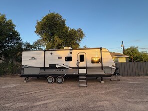 A recreational vehicle parked on a gravel surface with a ladder, a small window, and a door. - Cozy RV  close to bird sanctuary with chill vibes and fantastic sunset views. (San Ygnacio)