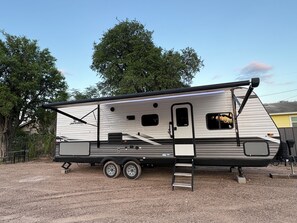 A recreational vehicle with a sliding door, a small window, and a ladder for access. - Cozy RV  close to bird sanctuary with chill vibes and fantastic sunset views. (San Ygnacio)