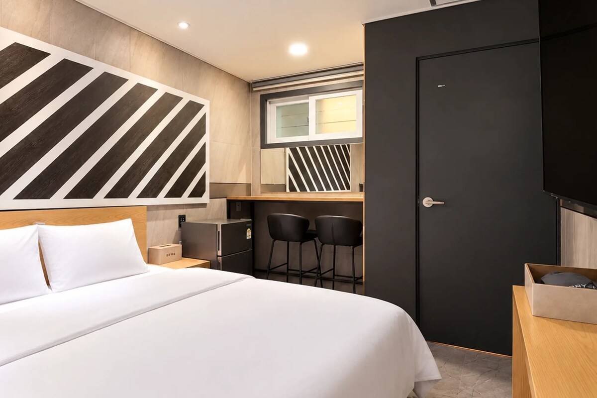 A hotel room with a bed, a desk with two chairs, a TV, and a door.
