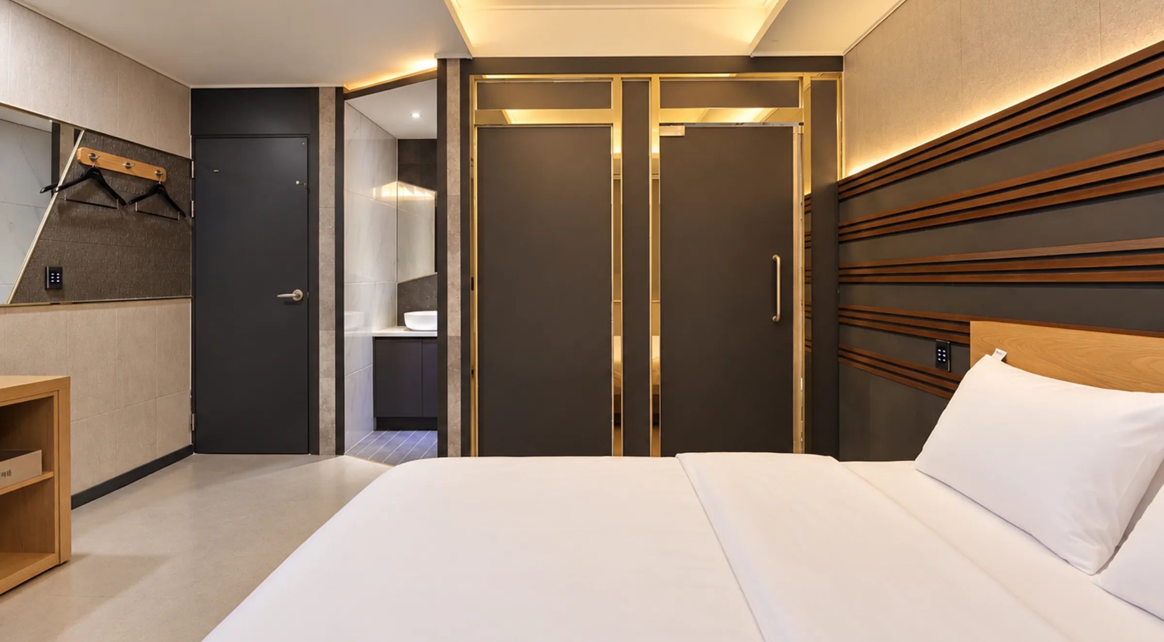 A hotel room with a bed, a wardrobe, a mirror, and a wooden shelf.
