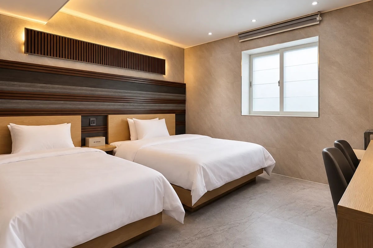 A hotel room with two beds, a desk, and a large window.