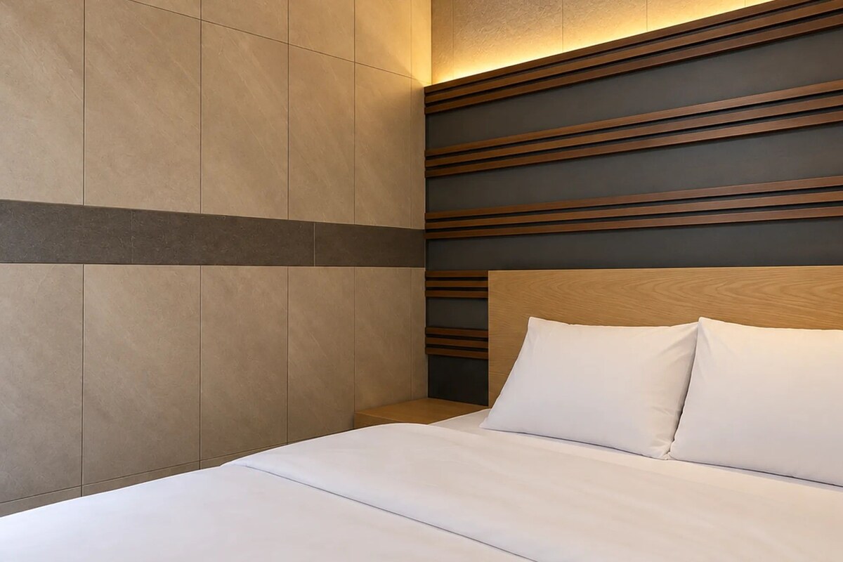 A modern hotel room with a wooden headboard, a large bed with white bedding, and a wall with horizontal wooden slats.