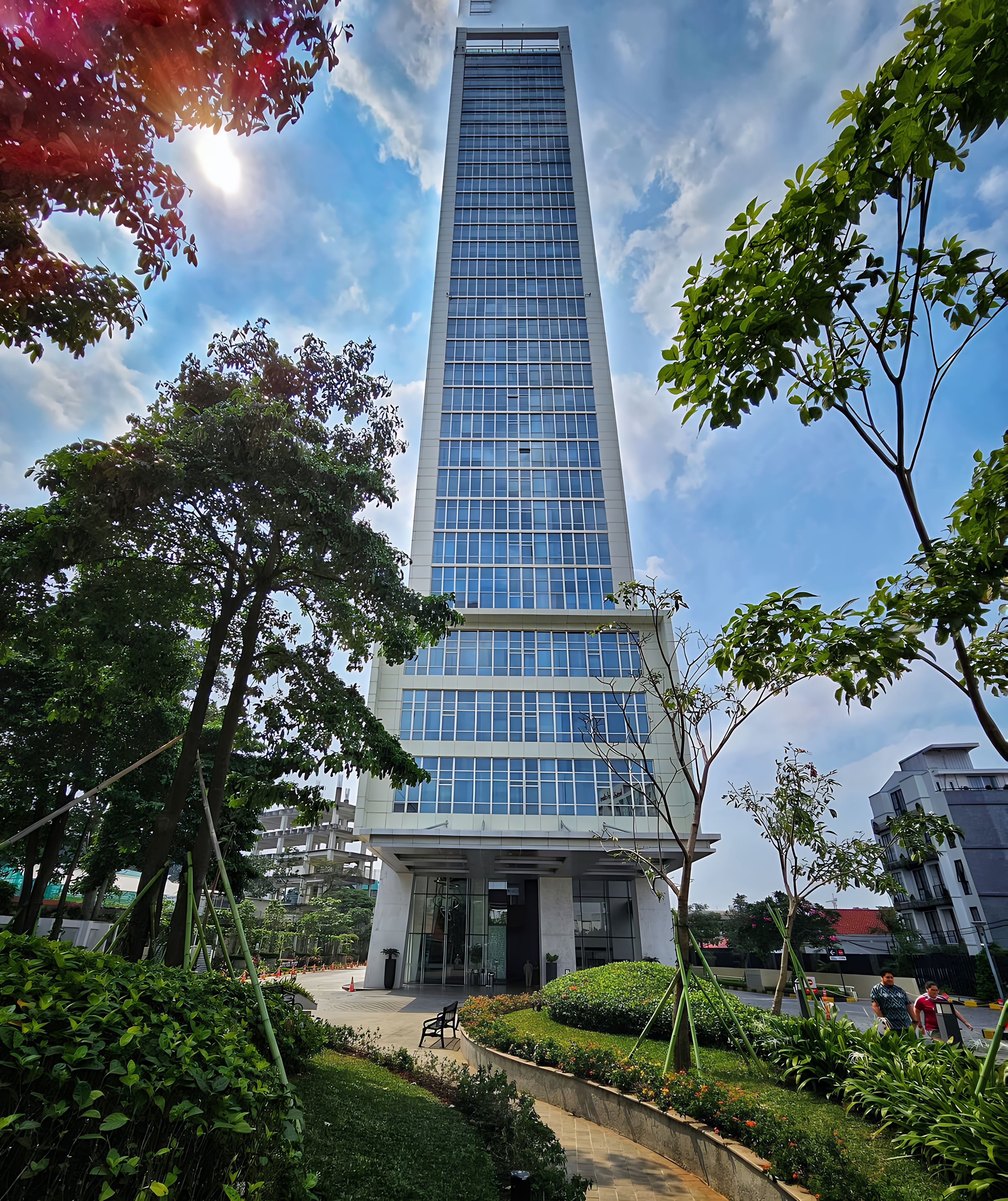 Un moderno edificio de gran altura con fachada de vidrio, rodeado de vegetación y un cielo despejado.