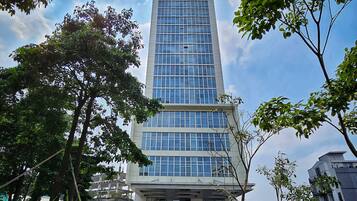 Un moderno edificio de gran altura con fachada de vidrio, rodeado de vegetación y un cielo despejado.