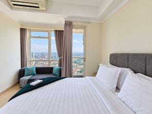 Habitación de hotel con una cama grande, un sofá, vista a la ciudad y una ventana con cortinas.