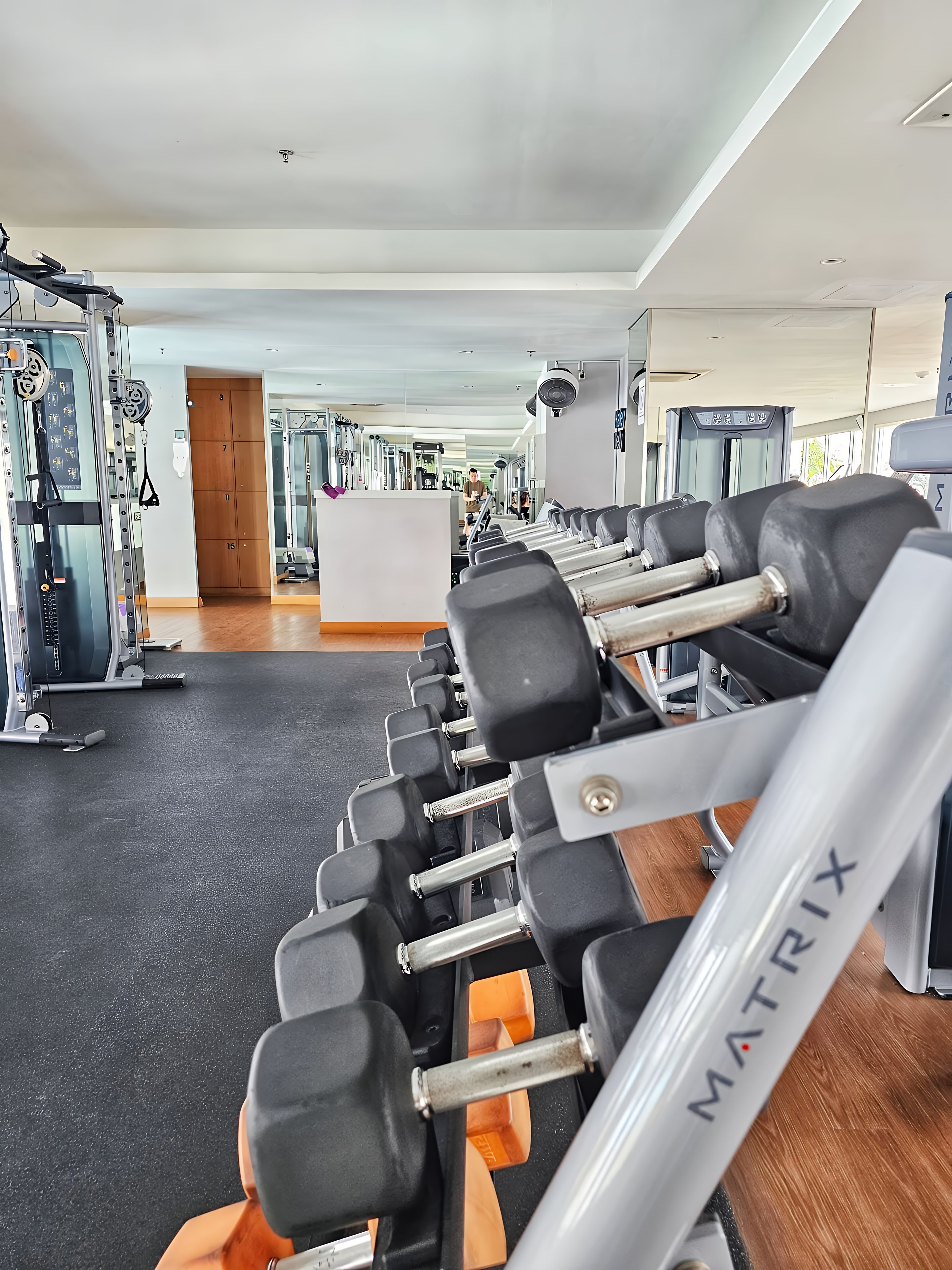 Un gimnasio con múltiples filas de mancuernas, máquinas de pesas y una pared de espejos.