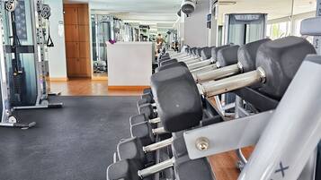 Un gimnasio con múltiples filas de mancuernas, máquinas de pesas y una pared de espejos.