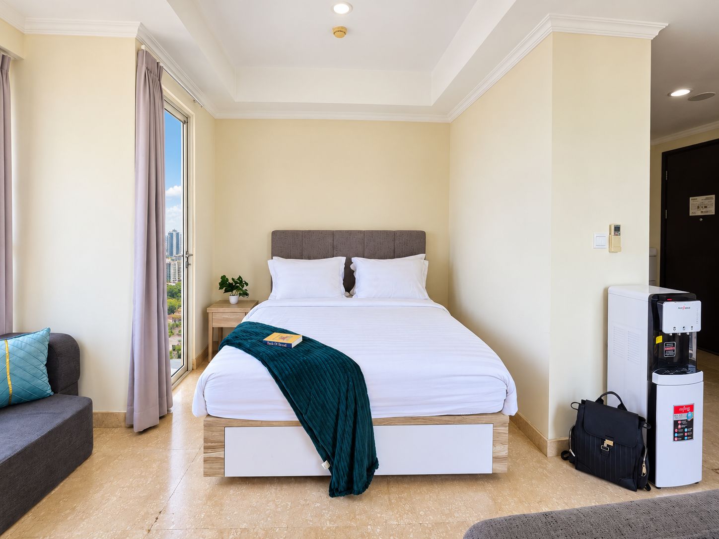 Habitación de hotel con cama, mesita de noche, cafetera y vista a la ciudad.