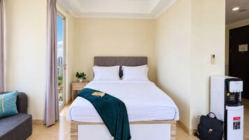 Habitación de hotel con cama, mesita de noche, cafetera y vista a la ciudad.