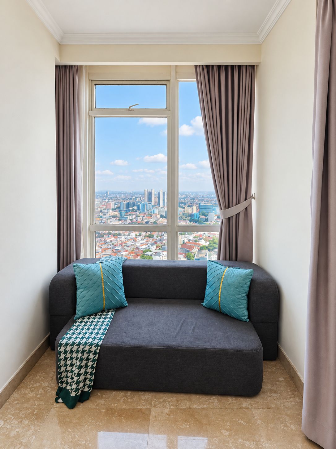 A corner room with a city view, a dark grey sofa with teal pillows, and a patterned throw.