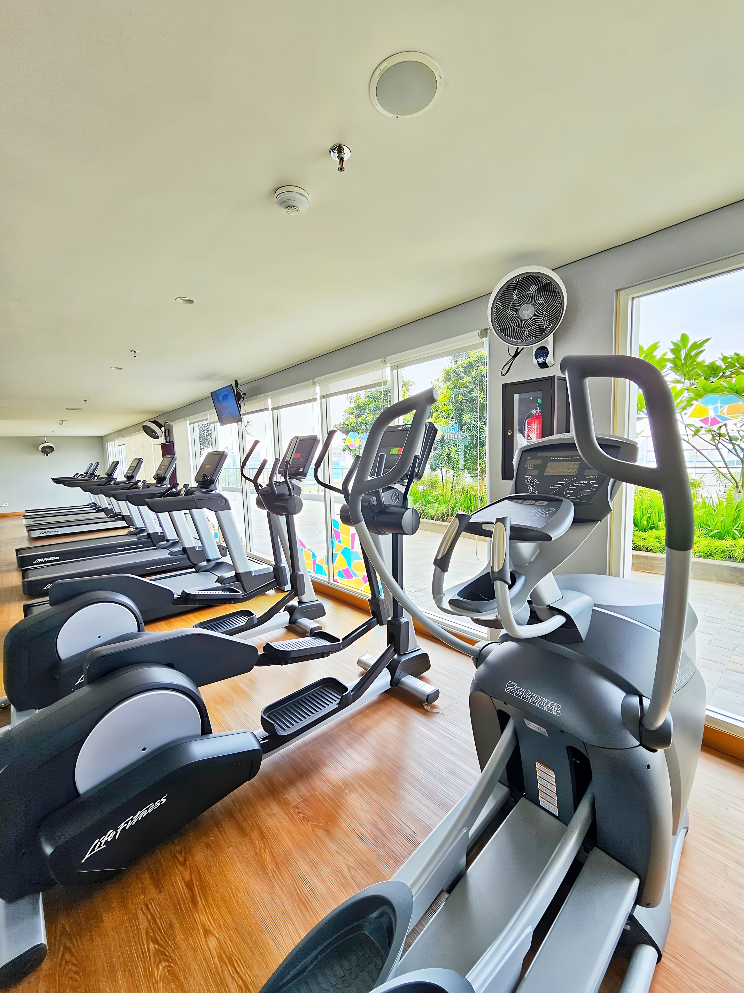 A gym with multiple treadmills, a fan, and a window with a view of greenery.