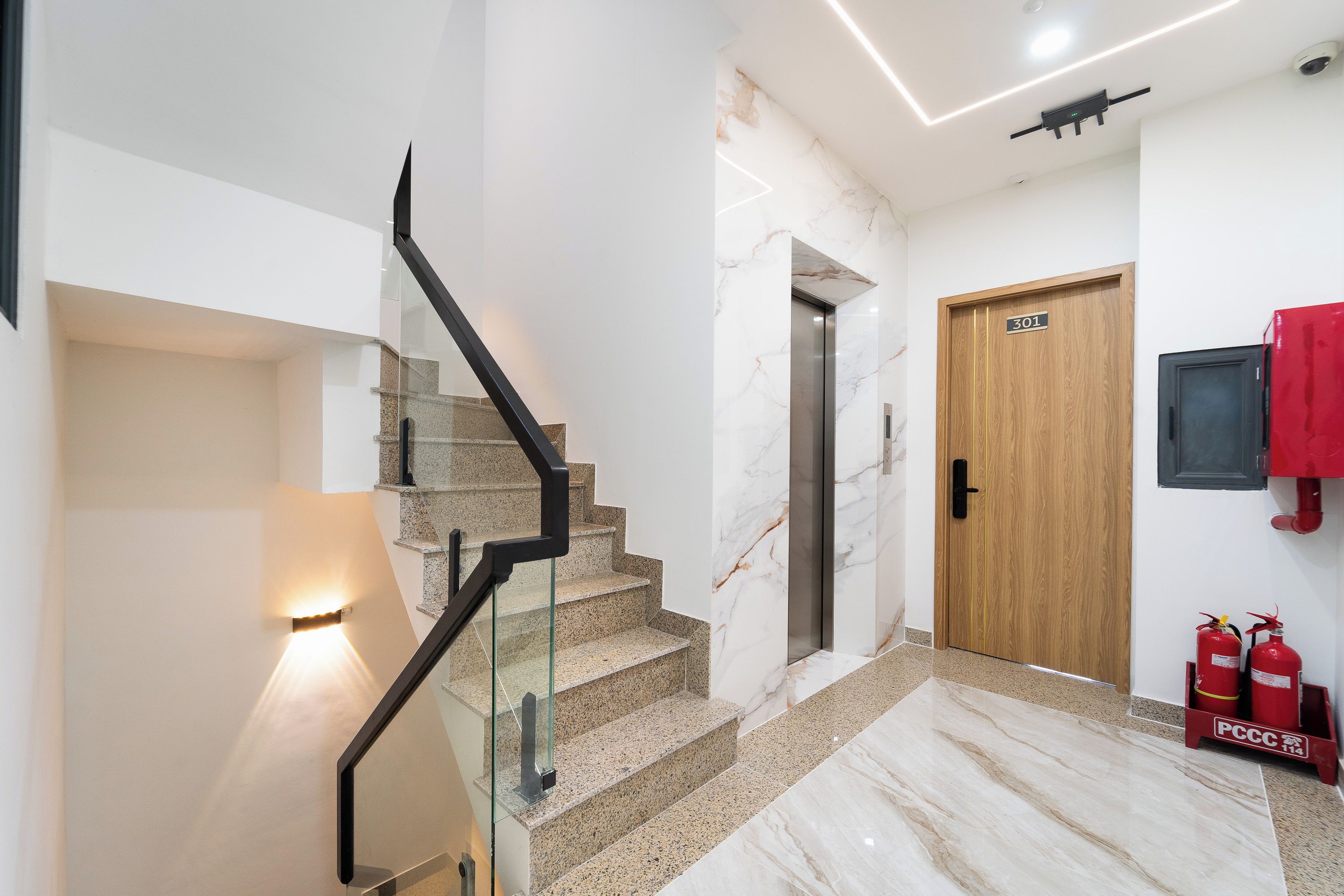 A modern interior with a glass railing staircase, a wooden door, and a fire extinguisher.
