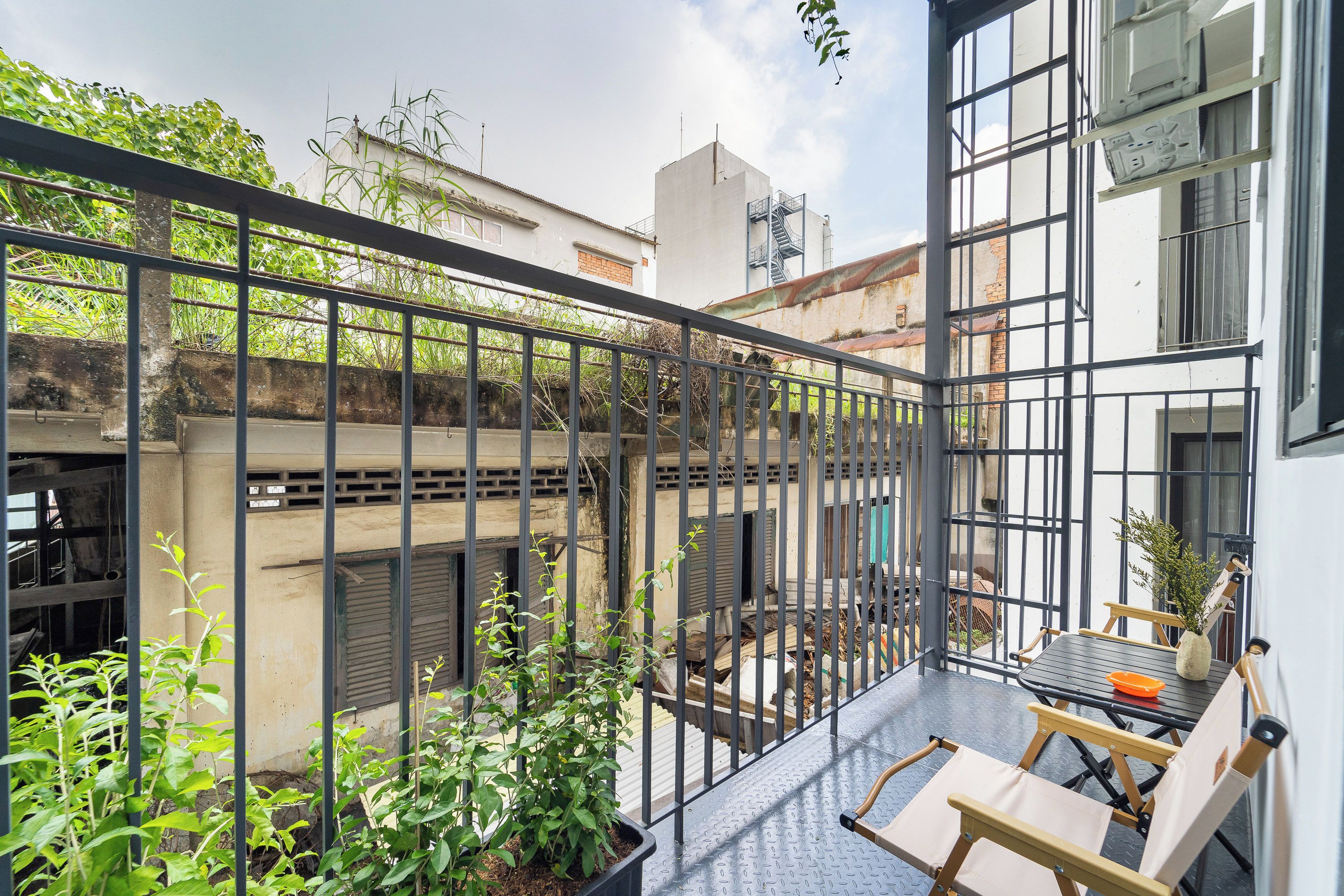 A balcony with a metal railing, a table with chairs, and potted plants.